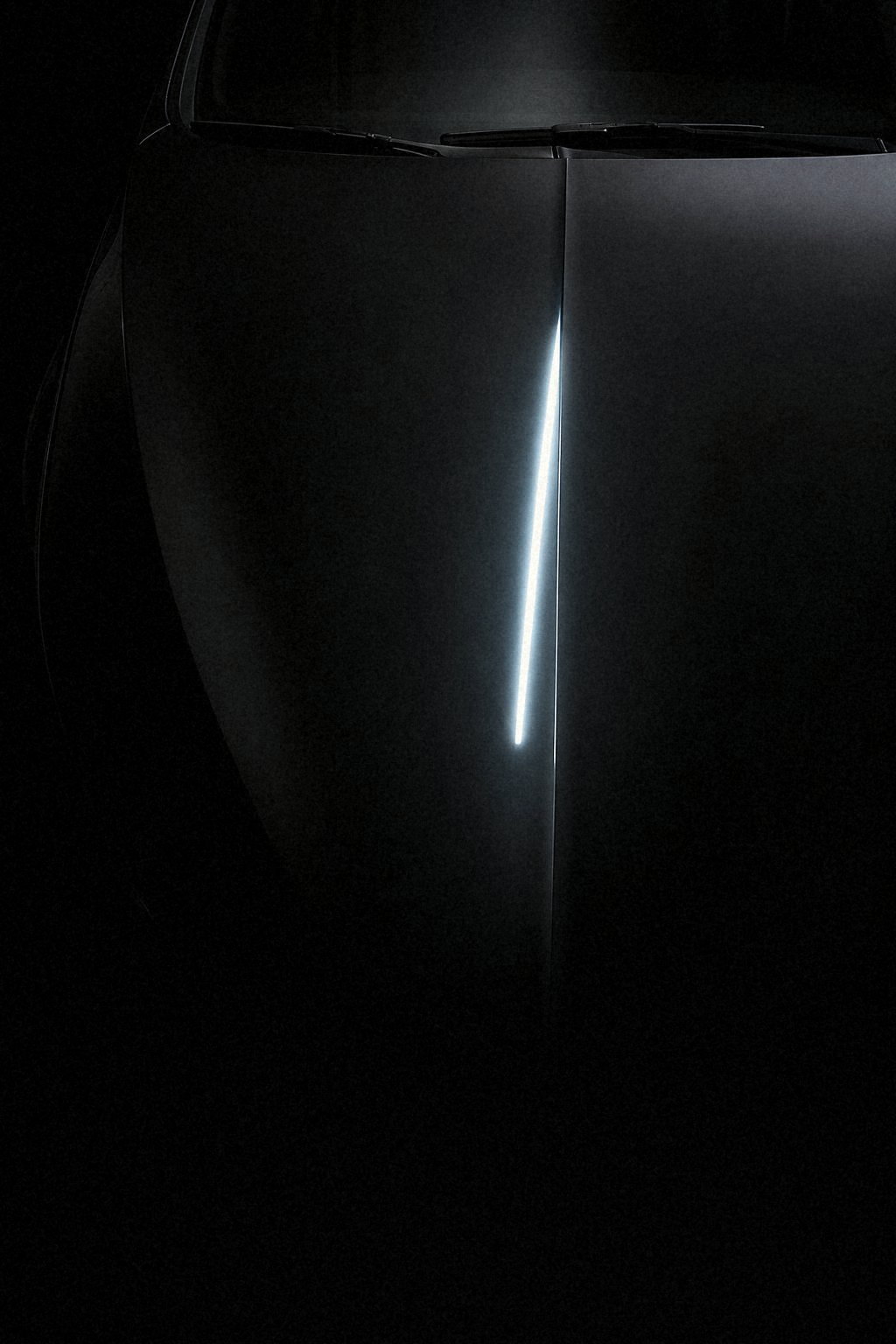 Looking down the centre crease of a black sedan hood at night, a single cool-white LED bar reflected as one narrow line that fades into darkness toward the nose